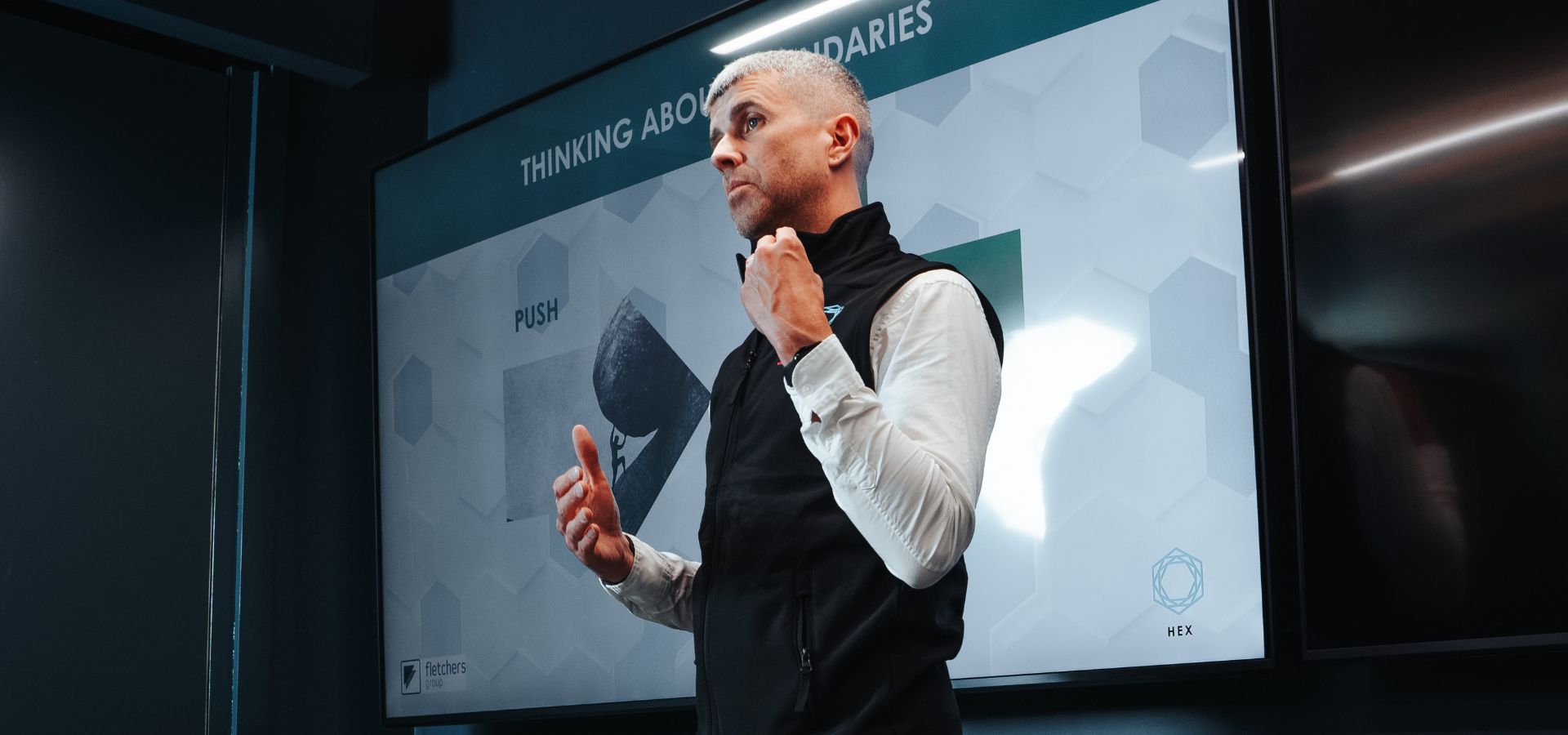 Tom Emery presenting at the front of a meeting room as part of his coaching programme for hr leaders. With a big screen and the words thinking about boundaries on the screen
