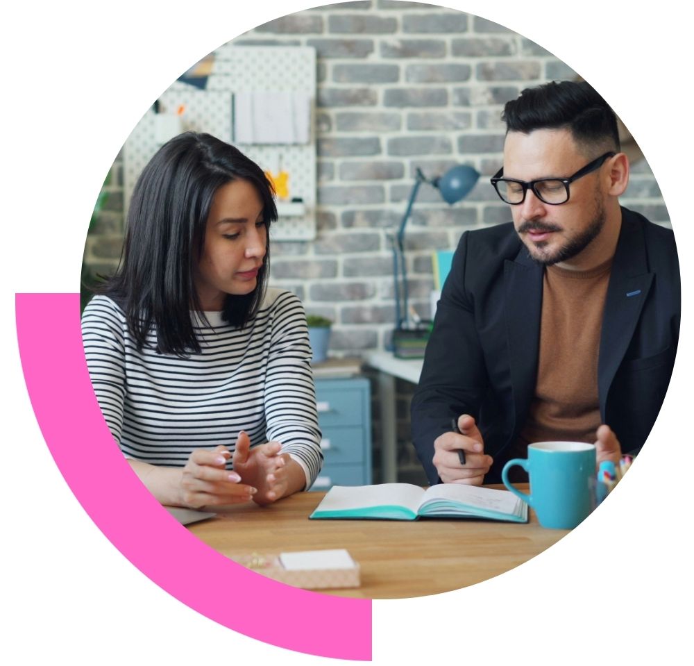 a man and a woman sat in a meeting room having a coaching session - the man is making notes in a note pad