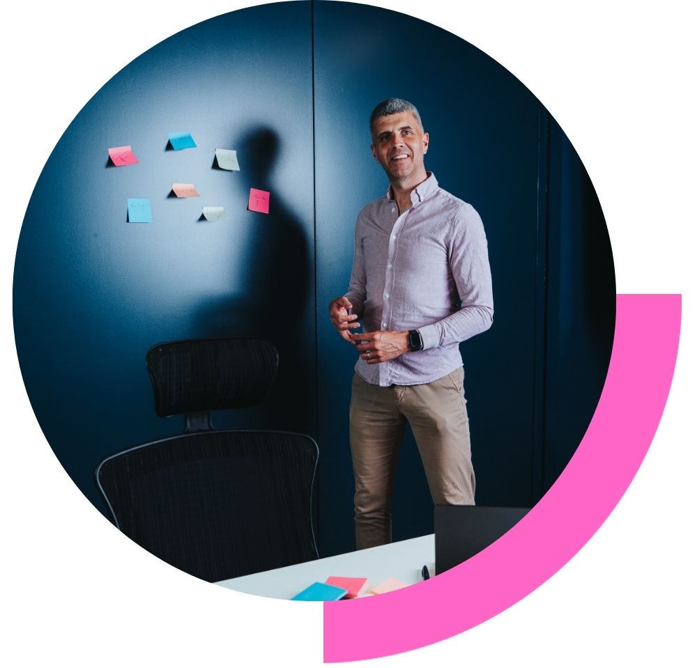 Tom Emery in a coaching session stood in a meeting room with lots of post it notes on the wall smiling