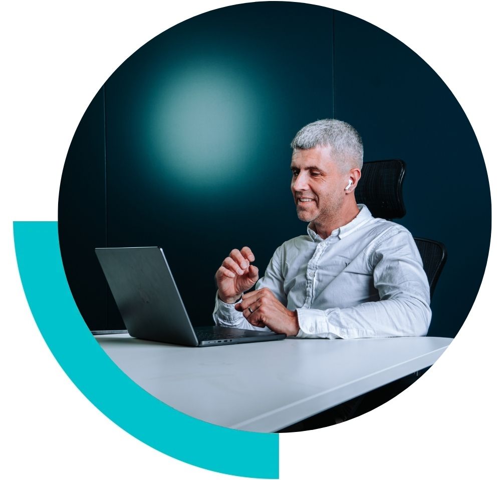 An image of Tom Emery sat at a desk. He is looking at an open laptop and smiling.